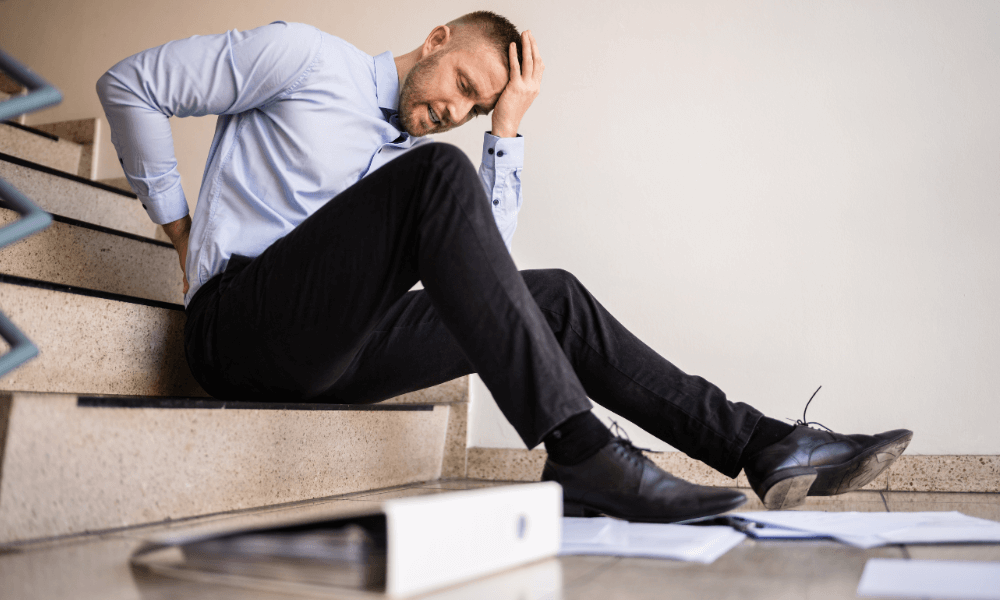 man sitting on a staircase holding his back after falling