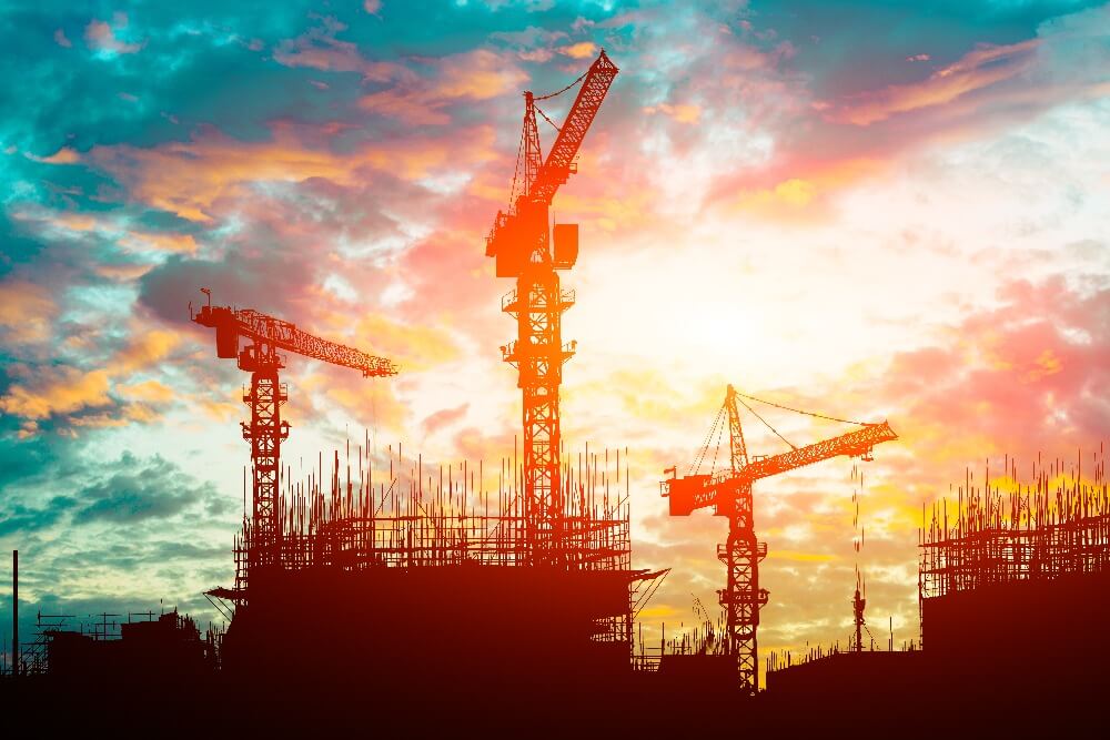 image of sunset with three cranes in foreground/silhouette 