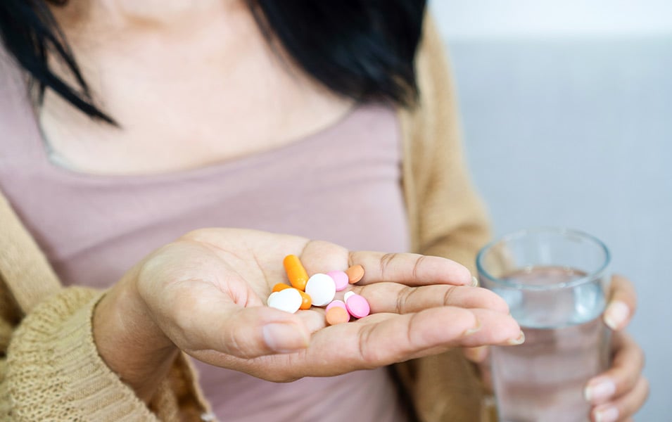 woman holding a hand full of pills and a glass of water